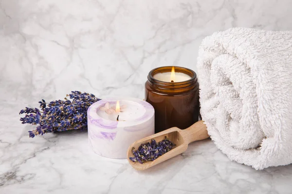 Lavender flowers and scented candle. The concept of spa, beauty and health salon, skin care cosmetics. Natural cosmetics.Aroma procedures. Closeup on white marble background.