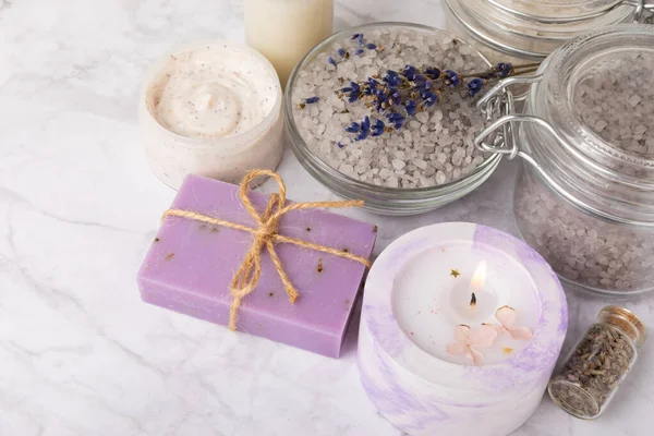 stock image Lavender flowers, fragrant sea salt, body cream and candle. The concept of spa, beauty and health salon, skin care cosmetics. Natural cosmetics.Aroma procedures. Closeup on white marble background.