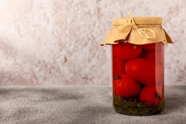 Canned pickled tomatoes in a jar on a marble background. Picking vegetables, harvesting. Canned pickled tomatoes. Preservation of tomatoes for the winter. Side view. Place for text. Place to copy.