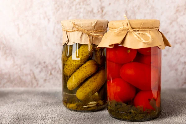 Canned pickled tomatoes and cucumbers in a jar on a marble background. Picking vegetables, harvesting. Canned pickled tomatoes and cucumbers. Preservation for the winter. Side view. Place for text.