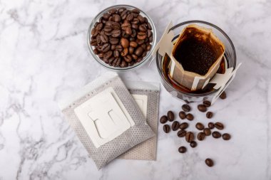 Evde kahve yapma modası. Kahverengi arka planda kahve çekirdekleri olan bir bardakta taze içecek damlatın. Fincanda demlenmek için öğütülmüş kahve. Kahveyi kağıt tipi filtre kullanarak damlat.