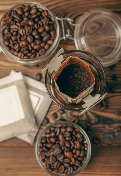Trends in making coffee at home. Drip bag of fresh drink in a glass with coffee beans on a brown background. Ground coffee for brewing in a cup. Drip coffee using a paper type filter.