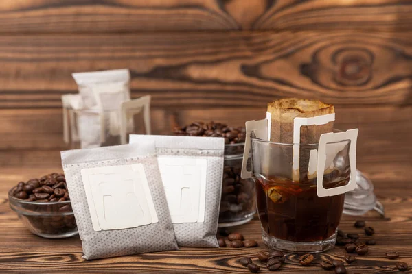 Trends in making coffee at home. Drip bag of fresh drink in a glass with coffee beans on a brown background. Ground coffee for brewing in a cup. Drip coffee using a paper type filter.