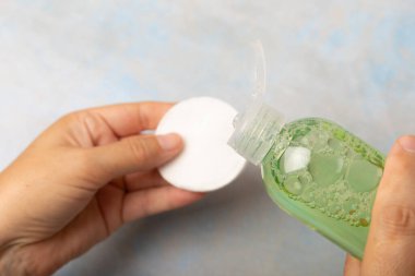 İçinde su bulunan bir şişe ve kadın ellerinde pamuk pedi. Makyaj çıkarıcı. Yüz temizleme ameliyatı. Güzellik konsepti. Cilt bakımı. Metin için yer.