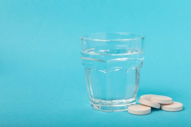 Öfkeli bir vitamin tableti mavi arka plandaki bir bardak suyun içinde düşer ve çözülür. Sağlık kavramı. Tıp konsepti. Metin için yer.
