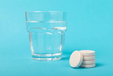 Öfkeli bir vitamin tableti mavi arka plandaki bir bardak suyun içinde düşer ve çözülür. Sağlık kavramı. Tıp konsepti. Metin için yer.
