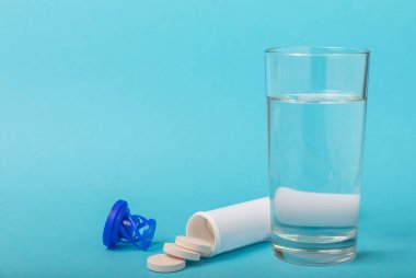Öfkeli bir vitamin tableti mavi arka plandaki bir bardak suyun içinde düşer ve çözülür. Sağlık kavramı. Tıp konsepti. Metin için yer.