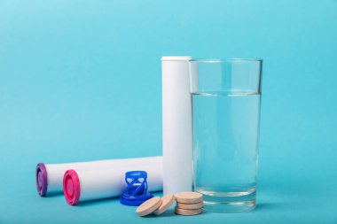 Öfkeli bir vitamin tableti mavi arka plandaki bir bardak suyun içinde düşer ve çözülür. Sağlık kavramı. Tıp konsepti. Metin için yer.