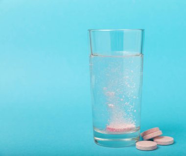 Öfkeli bir vitamin tableti mavi arka plandaki bir bardak suyun içinde düşer ve çözülür. Sağlık kavramı. Tıp konsepti. Metin için yer.