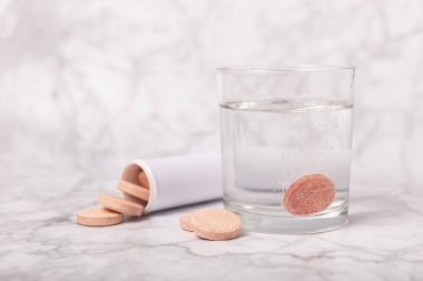 Portakal aromalı C vitamini hapları beyaz mermer arka planda bir bardak suda erir. Sağlık kavramı. Tıp konsepti. Metin için yer.