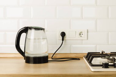 Mutfaktaki masada kaynar su bulunan şeffaf elektrikli su ısıtıcısı. Kaynar su, çay ve kahve yapmak için çaydanlık. Sıcak içecek yapmak için ev aletleri..
