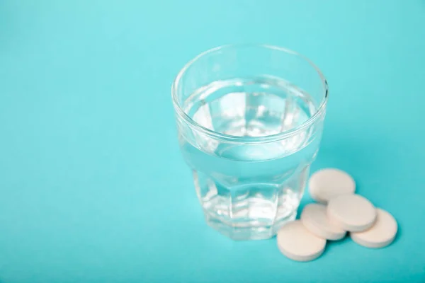 stock image An effervescent vitamin tablet drops and dissolves in a glass of water on a blue background. The concept of health. Medicine concept. Place for text.