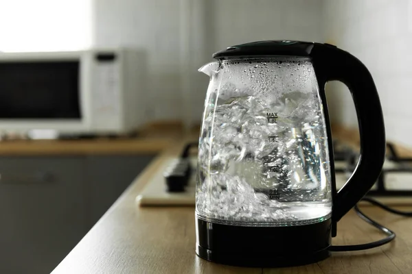 Transparent electric kettle with boiling water on the table in the kitchen.Kettle for boiling water and making tea and coffee.Home appliances for making hot drinks.