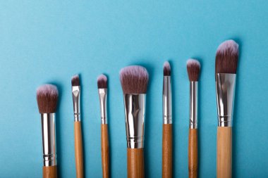 Mavi arka planda makyaj için makyaj fırçası. Makyaj için kozmetik ürün. Yaratıcı ve güzel moda konsepti. Moda. Kozmetik makyaj fırçası koleksiyonu, üst görüş, afiş. Mesaj için yer. MOCAP.