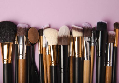 Eflatun arka planda makyaj için makyaj fırçası. Makyaj için kozmetik ürün. Yaratıcı ve güzel moda konsepti. Moda. Makyaj fırçası koleksiyonu, üst görünüm, afiş. Metin için yer.