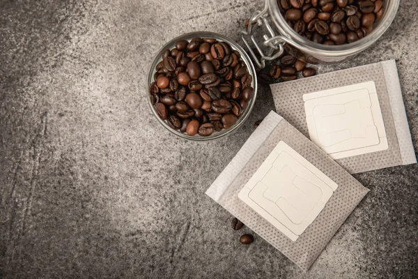 Drip coffee bag and coffee beans, ground coffee for brewing in a cup, paper bag drip coffee filter packaging. composition on a black marble texture table.MOCAP. The concept of brewing a drink.