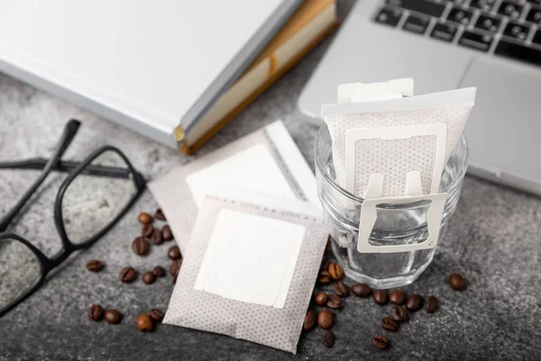 Drip coffee bags, coffee beans and a glass cup on a texture table. Ground coffee for brewing in a cup, paper bag drip coffee filter packaging. Place to copy. Place for text.