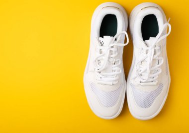 Sarı arka planda bir çift beyaz ayakkabı. Beyaz şık ayakkabılar. STREET STYLE.Sports konsepti, unisex, spor ayakkabıları, yaşam tarzı, konsept, ürün fotoğrafı, havalanma konsepti, sokak giyimi.