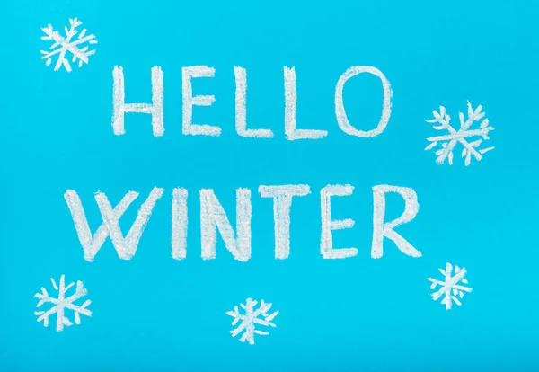 Chalk lettering HELLO WINTER on a blue textural background. Snowflakes