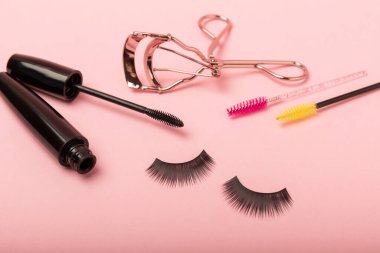 Takma kirpikler, rimel ve kirpik fırçaları, pembe arka planda kirpik bigudileri. Makyaj aletleri. Güzellik konsepti. Makyaj. Mesaj için yer. Kopyalama yeri. Düz çizgi. MOCAP.