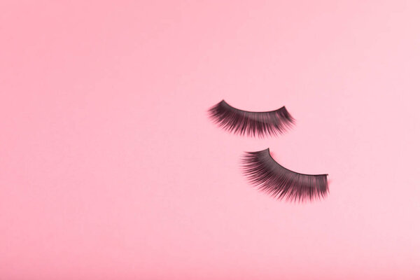 Ложные ресницы на розовом фоне. Флэтли. Концепция красоты и моды. Расширение ресниц. индустрии красоты. Место для смс. Место для копирования.