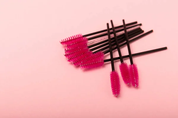 Eyelash extension brushes on a pink background. Brush for combing extended and false eyelashes. Brush for straightening eyelashes and eyebrows.