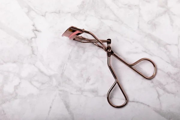 Eyelash curler on a white marble background. Curling tweezers and false eyelashes. Beauty concept. Makeup tool. Place for text. Place to copy. Mocap. FLETLEY.