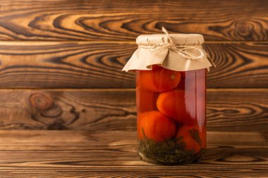 Kahverengi desenli kırsal ahşap üzerinde cam bir kavanozda kırmızı kiraz domatesleri turşusu. Sonbahar ya da kış için gıda korunumu. Ev deposu. Konserve, fermantasyon konsepti. Mesaj için yer. Boşluğu kopyala.