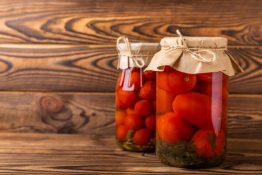 Kahverengi desenli kırsal ahşap üzerinde cam bir kavanozda kırmızı kiraz domatesleri turşusu. Sonbahar ya da kış için gıda korunumu. Ev deposu. Konserve, fermantasyon konsepti. Mesaj için yer. Boşluğu kopyala.