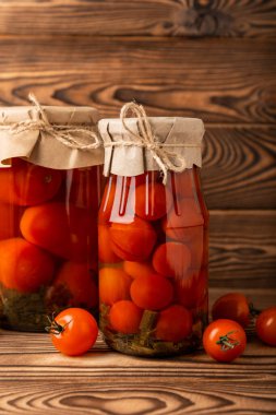 Kahverengi desenli kırsal ahşap üzerinde cam bir kavanozda kırmızı kiraz domatesleri turşusu. Sonbahar ya da kış için gıda korunumu. Ev deposu. Konserve, fermantasyon konsepti. Mesaj için yer. Boşluğu kopyala.