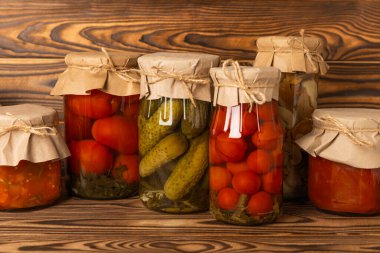 Kahverengi ahşap arka planda salatalık, domates, mantar ve patlıcan kavanozları. Turşu ve konserve yiyecekler. Uzayı kopyala Metin için yer.