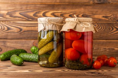 Kırsal ahşap bir arka planda salatalık ve domates kavanozları. Turşu ve konserve yiyecekler. Uzayı kopyala Metin için yer.
