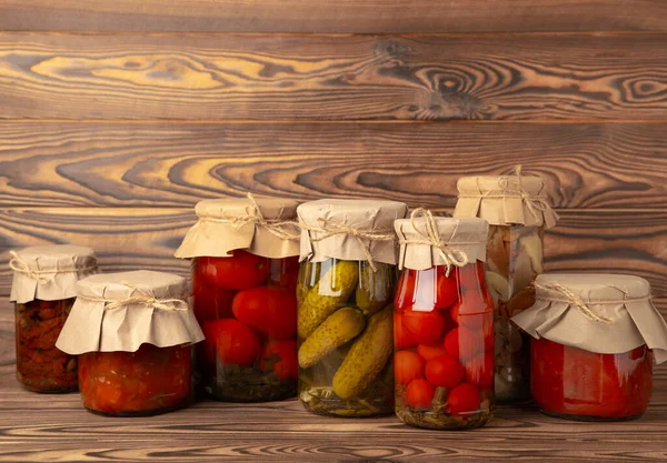 Jars of pickled vegetables cucumbers, tomatoes, mushrooms and eggplant on a brown wooden background. Pickled and canned foods. Copy space. Place for text.