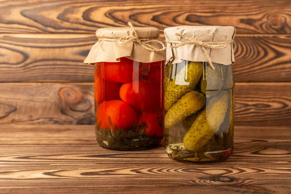 Jars of pickled vegetables cucumbers and tomatoes on a rustic wooden brown background. Pickled and canned foods. Copy space. Place for text.