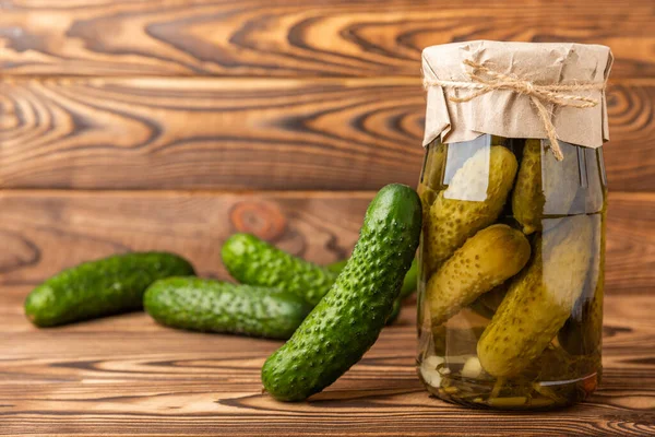 Canned pickled cucumbers in a glass jar on a brown textural background. Pickles. Canning, fermentation concept. Place for text. Copy space.