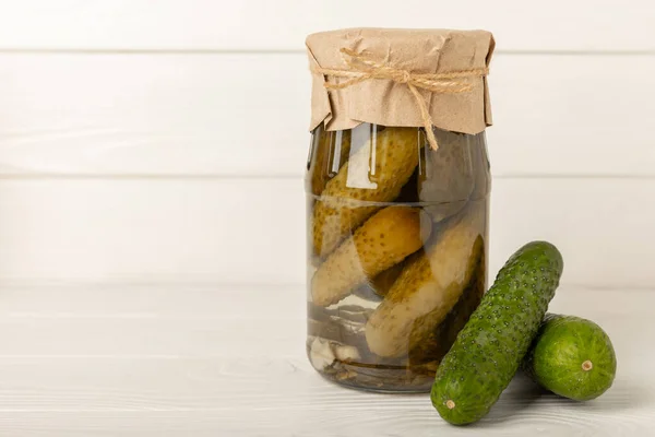 Canned pickled cucumbers in a glass jar on a white texture background. Pickles. Canning, fermentation concept. Place for text. Copy space.