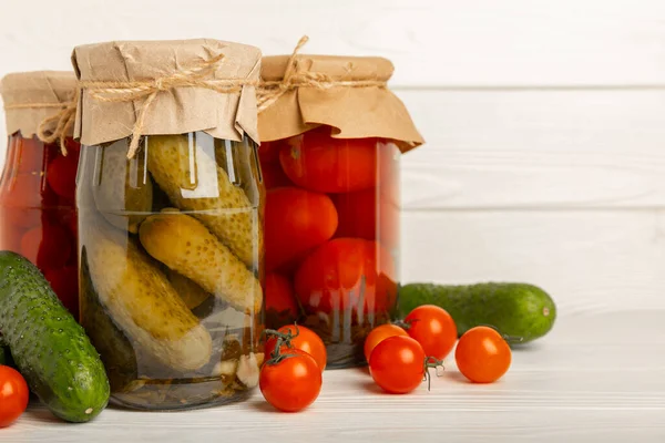 Jars of pickled vegetables cucumbers and tomatoes on a rustic wooden white background. Pickled and canned foods. Copy space. Place for text.