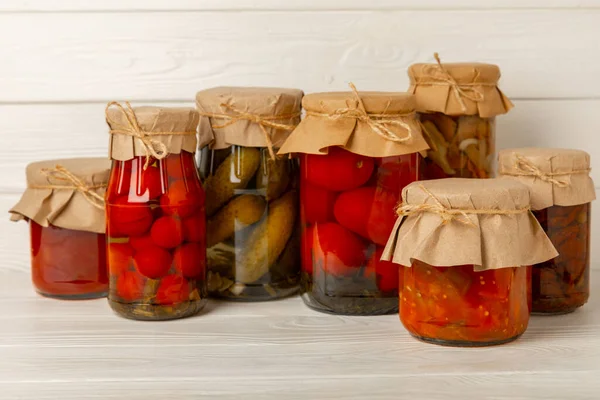 Jars of pickled vegetables cucumbers, tomatoes, mushrooms and eggplants on a light textural background. Pickled and canned foods. Copy space. Place for text.