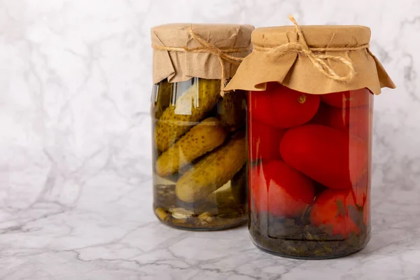 Jars of pickled vegetables cucumbers and tomatoes on a marble background. Pickled and canned foods. Copy space. Place for text.
