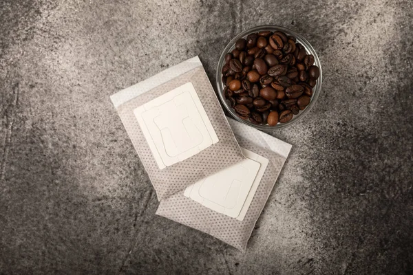 Drip coffee bag and coffee beans, ground coffee for brewing in a cup on a black marble background.Filter for drip coffee. Flatley. Copy space. Place for text.