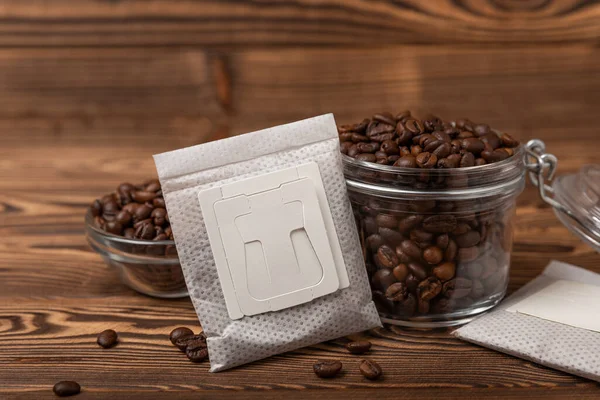 Drip coffee bag and coffee beans, ground coffee for brewing in a cup on brown texture wood.Drip coffee filter. Flatley. Copy space. Place for text.