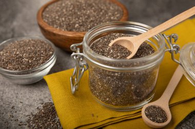 Kaşık içinde Chia tohumu ve siyah dokuda kase. Süper yiyecek ve aksiyoner. Diyet olsun. Yakın plan. Mesaj için yer. Boşluğu kopyala.