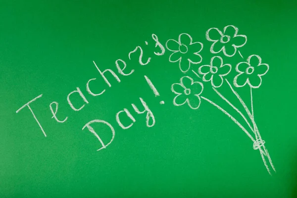 Chalk lettering TEACHER\'S DAY and a bouquet of flowers on a green blackboard. Concept Teacher\'s Day.