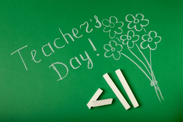 Chalk lettering TEACHER\'S DAY and a bouquet of flowers on a green blackboard. Concept Teacher\'s Day.