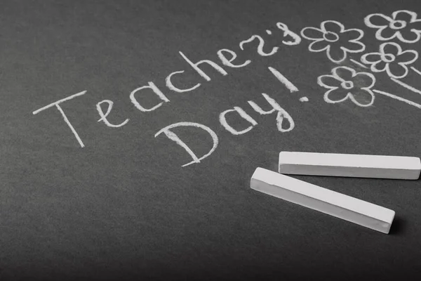 Chalk lettering TEACHER\'S DAY and a bouquet of flowers on a black chalkboard. Concept Teacher\'s Day.