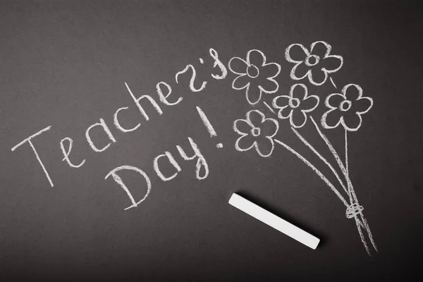 Chalk lettering TEACHER\'S DAY and a bouquet of flowers on a black chalkboard. Concept Teacher\'s Day.