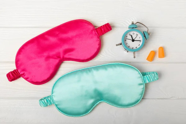Sleep mask, alarm clock, earplugs and sleeping pills on a white texture background.Top view.FLETLEY. The concept of restful and sound sleep. Insomnia.