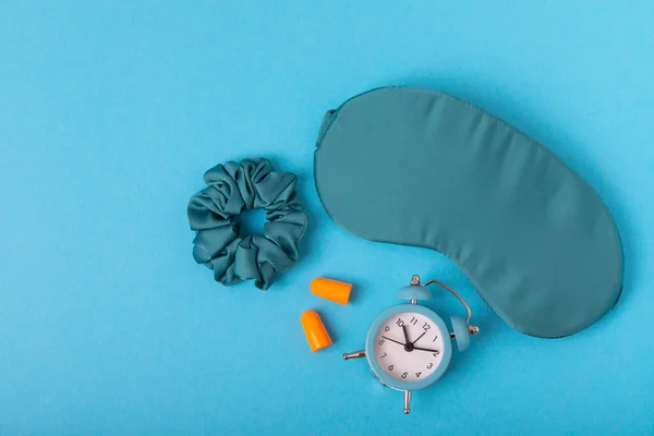 Sleep mask, alarm clock, earplugs and sleeping pills on a blue textural background.Top view.FLETLEY. The concept of restful and sound sleep. Insomnia.