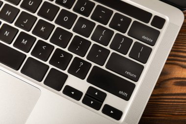 Gümüş arka planda siyah düğmeli dizüstü bilgisayar klavyesi. Kahverengi ahşap bir masada dizüstü bilgisayar. Modern bir dizüstü bilgisayarın klavyesi.