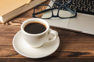 Laptop, kahve fincanı, gözlük, not defteri ve kalem, ofis konsepti. İş konsepti. Evde çalış. Bilgisayarlı çalışma alanı. Mocap. Mesaj için yer. Boşluğu kopyala.